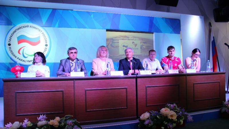 Seven members of the Russian Paralympic Comittee sitting at a desk at a press conference. 