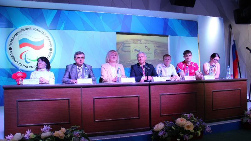 Seven members of the Russian Paralympic Comittee sitting at a desk at a press conference. 