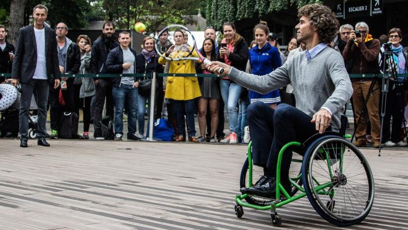 An athlete in a wheelchair hitting a ball with a tennis racket. 