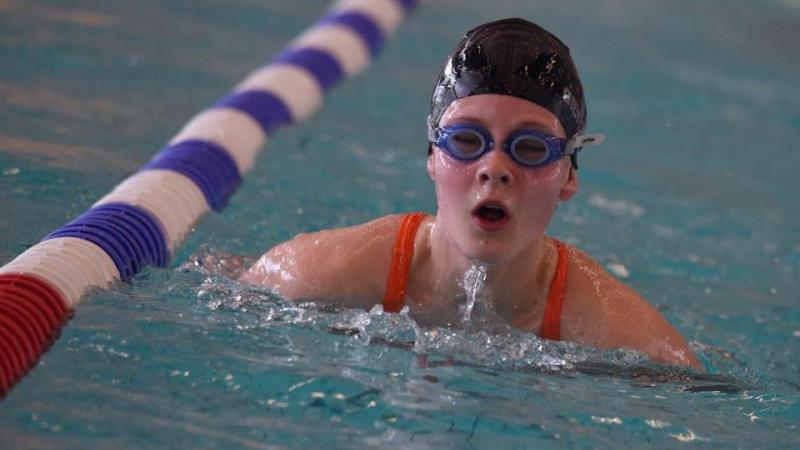 Girl swimming in the pool with swimcap and goggles on. 