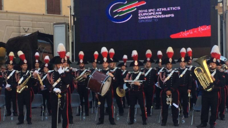 Music band of uniformed men in front of a TV board