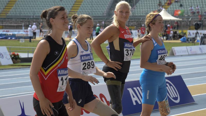 Group of women with leg prosthetics standing in a stadium, one is looking into the camera