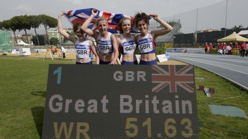 Four girls with British flag post behind a scoreboard