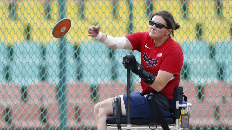 Woman sits in chair and throws discus