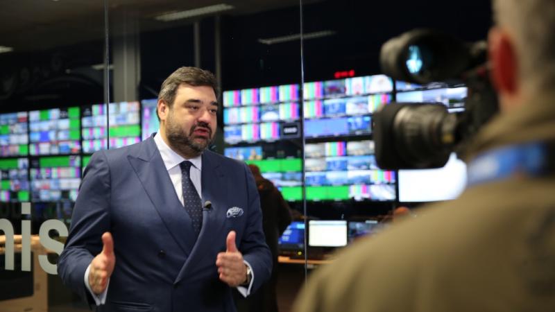 Man in suit being filmed in front of many monitors