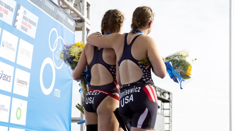 Three Para triathlete women on the podium while the US flag is being raised