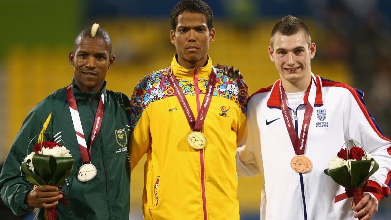 Colombian athlete Dixon Hooker poses on the podium with his gold medal next to the silver and bronze medallists.
