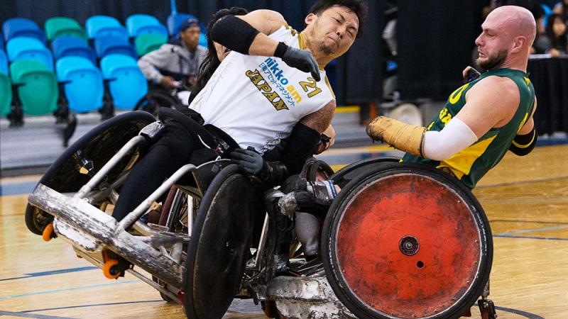 Two men playing wheelchair rugby collide their chairs. 