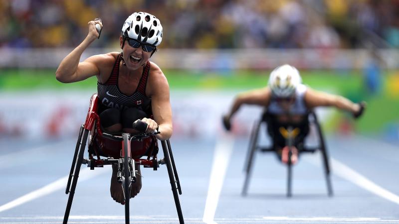 Woman in racing wheelchair crossing a finish line, celebrating