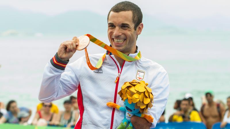 man stands on podium holding up a medal and a mascot