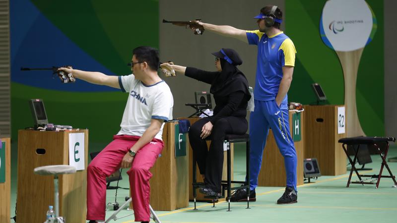 Two sitting and one standing shooting para athlete aiming at the targets