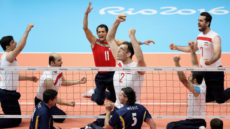 Group of sitting volleyball players celebrate after a point. 