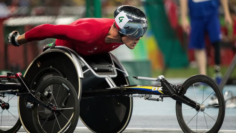 Close up of a wheelchair racer with a red racing suit and a silver helmet.