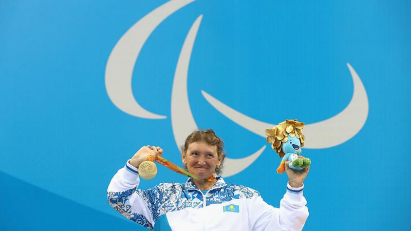 Woman on podium in a wheelchair, showing a medal