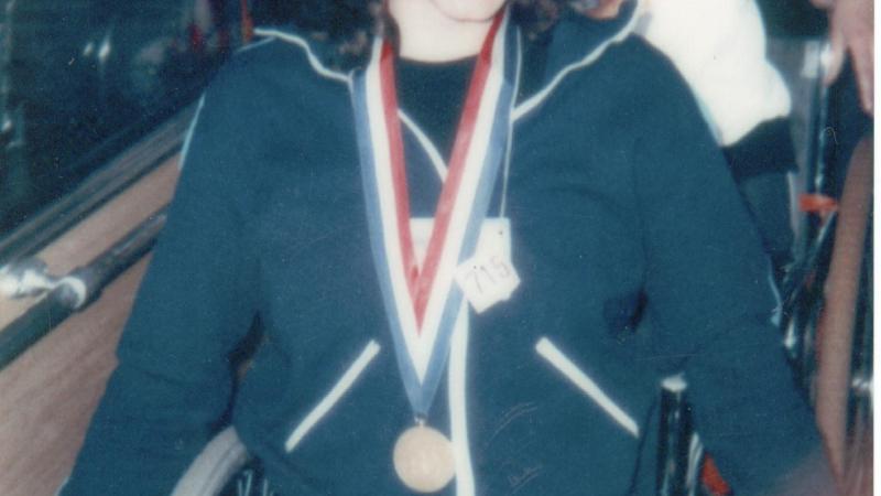 Photo of a woman in a wheelchair with a medal around her neck. The photo looks very old