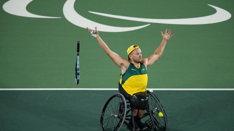 man in wheelchair throws away his tennis racket and raises his arms to celebrate