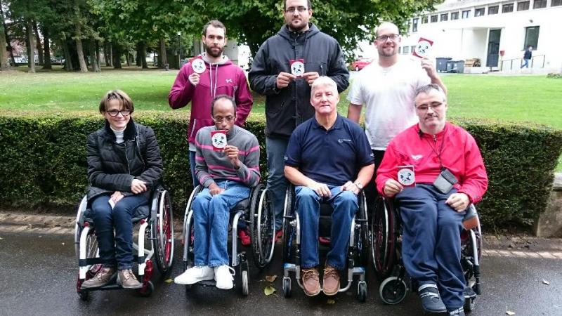 Five people in wheelchairs and standing pose with certificates