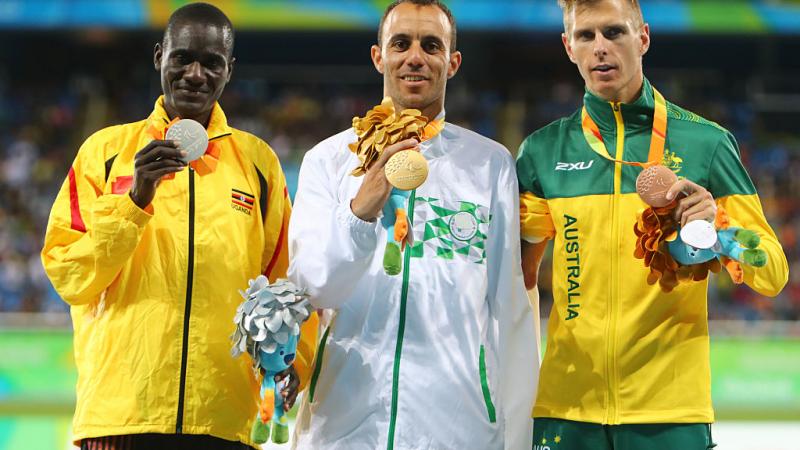 Uganda's track and field athlete David Emong celebrates on the podium with the gold and bronze medallists.