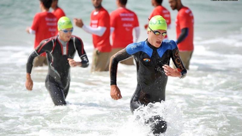 Two men in wet suits coming out of the water