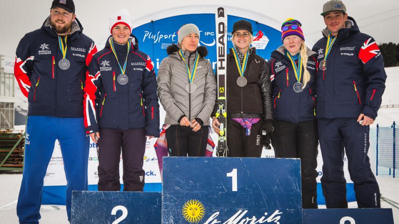 Three female alpine skiers and their guides standing on the podium
