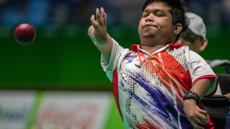 Upper body of man in wheelchair throwing a red ball