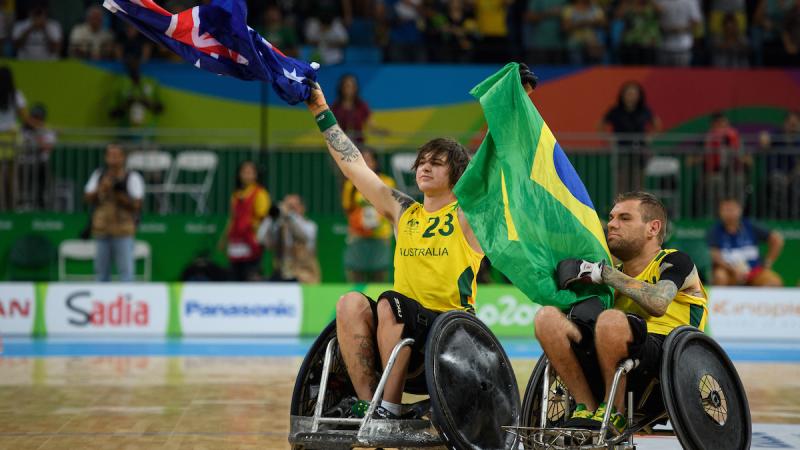 Two men in wheelchairs raise Australian and Brazilian flags. 