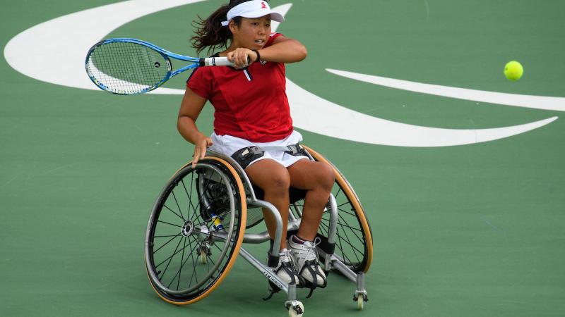 A Japanese wheelchair tennis player is hitting the ball.