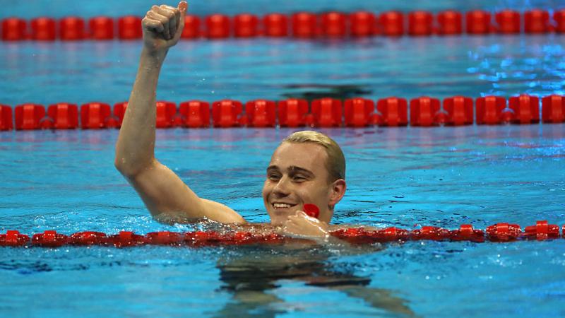 A swimmer celebrating his gold medal in the water, raising one arm.