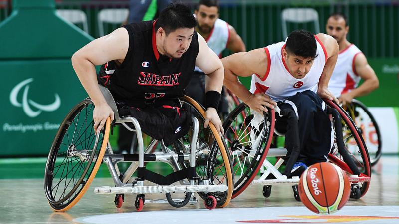 Two men in wheelchairs chasing a basketball