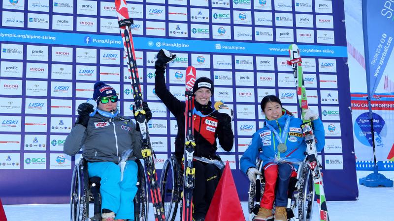 Three women in wheelchairs raising their arms with medals