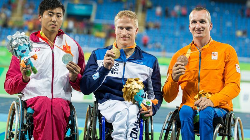 Three men in wheelchairs on a podium showing their medals