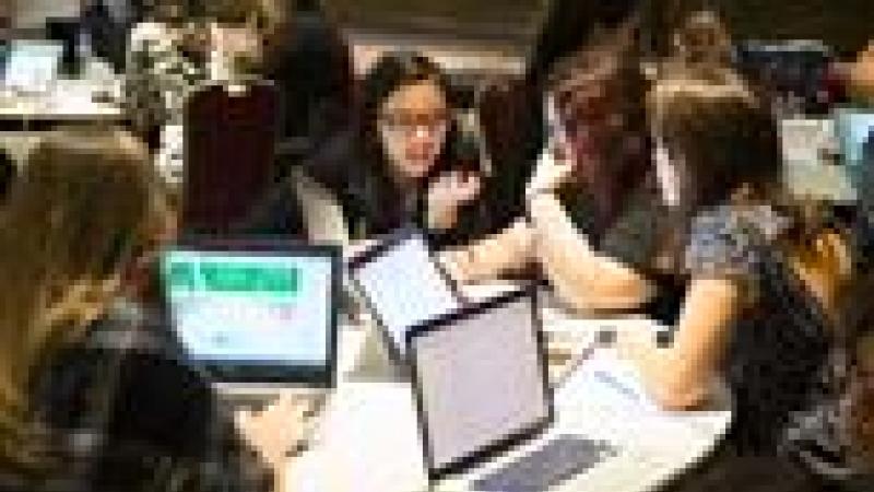 Group of young people sitting around a table with laptops, discussing