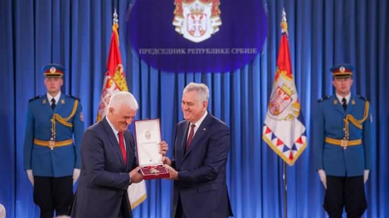 Two men on a stage, one handing a medal to the other