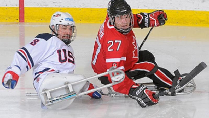 A picture of two men in sledges playing ice hockey