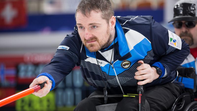Man in blue training suit and in wheelchair focusing on something behind the camera