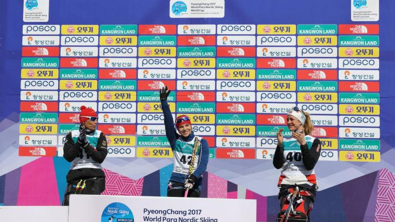 A sit skier raises her arm in the air to celebrate her victory