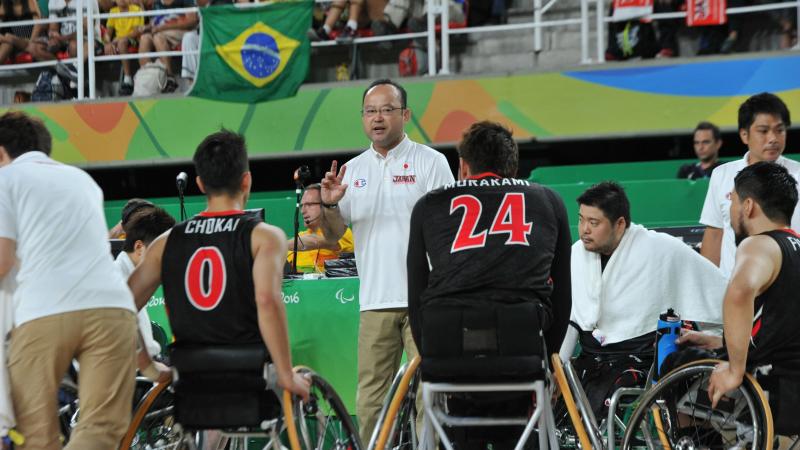 Coach surrounded by his men's wheelchair basketball team giving instuctions 