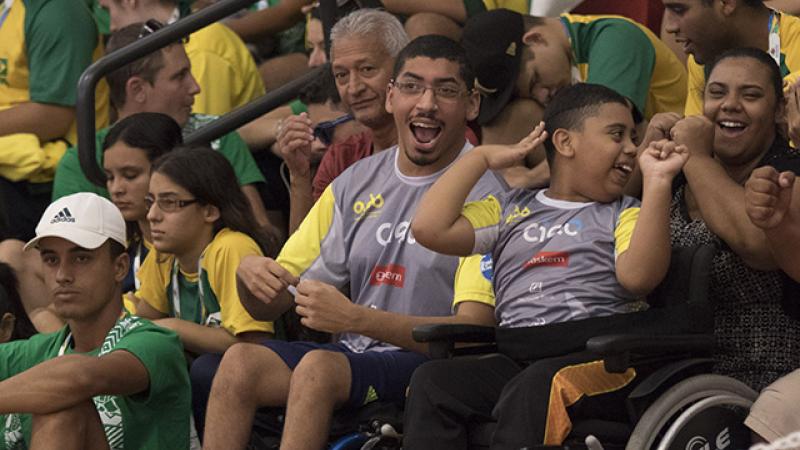 A man and a boy in a wheelchair watch a wheelchair basketball competition
