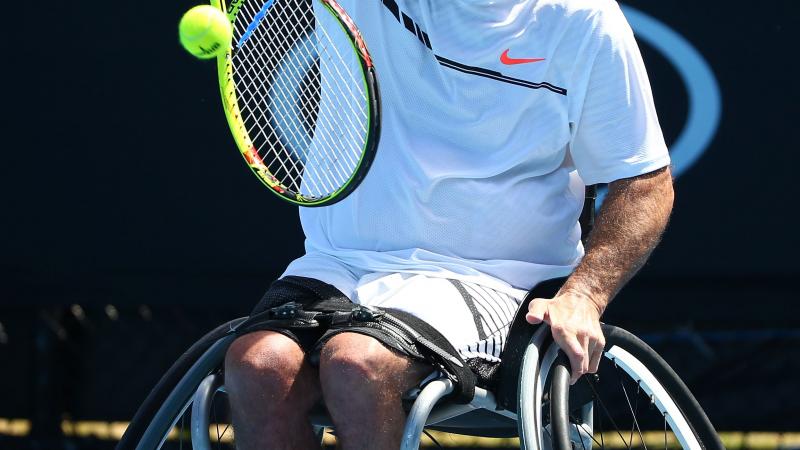 Man in wheelchair returns a tennis ball