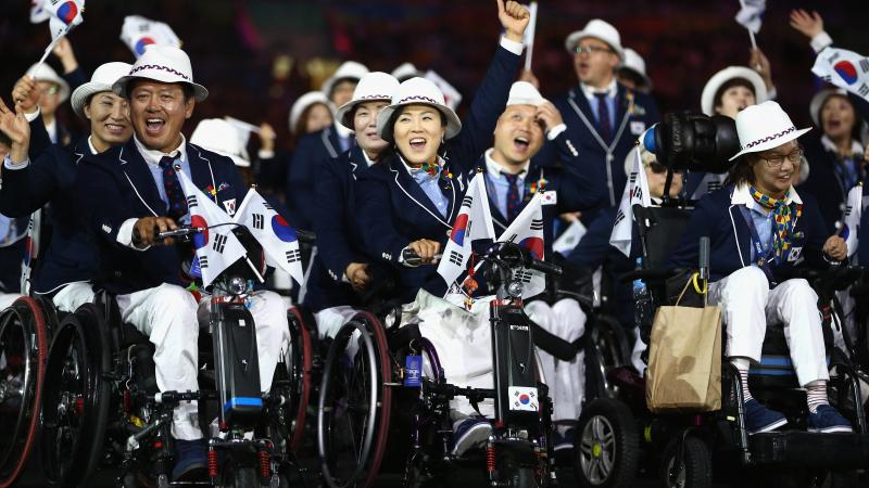 South Korean athletes in wheelchairs hold flags as they enter the stadium