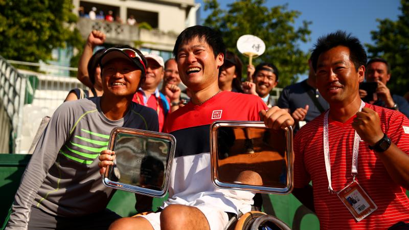 Man in wheelchair holds trophies with two other men next him.