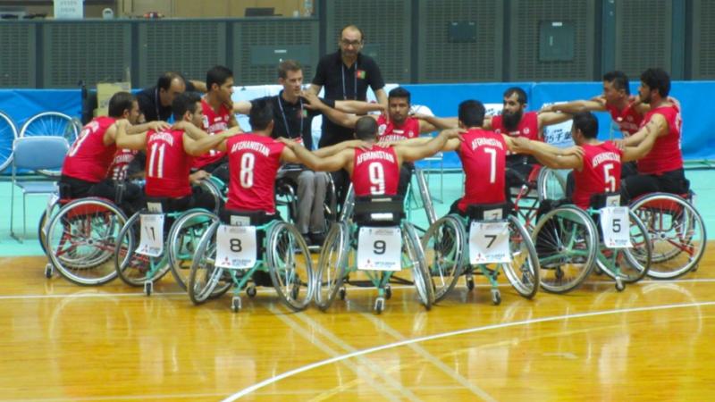 Men in basketball wheelchairs huddle around each other