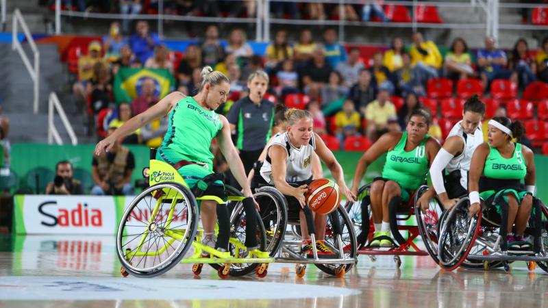 Woman in wheelchair goes for loose basketball while oppents guard her