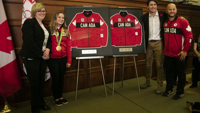Four people stand between two signed jerseys, posing for a photo
