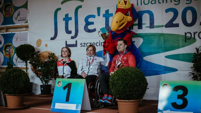 Three shooters on a podium with event mascot