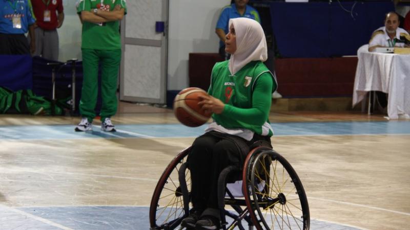 Woman wearing a hijab shooting a basketball in a wheelchair
