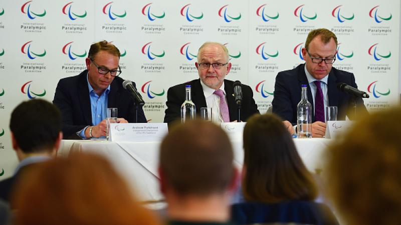 Three men sit at podium during press conference