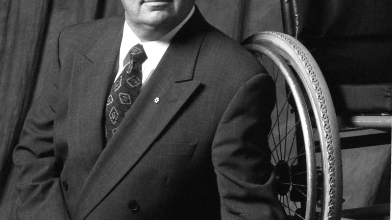 Black and white portrait of a man sitting infront of a wheelchair 