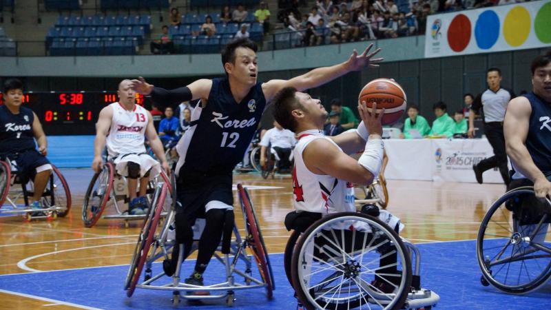 Man in wheelchair tries to block another man in wheelchair playing basketball