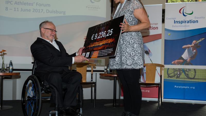 IPC Athletes' Forum - Elvira Stinissen and Sir Philip cheque Woman presents man in wheelchair with a cheque